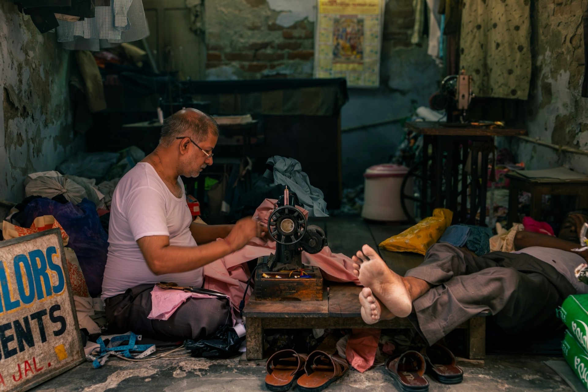 A tailor stitching pink fabric on a sewing machine in a small workshop