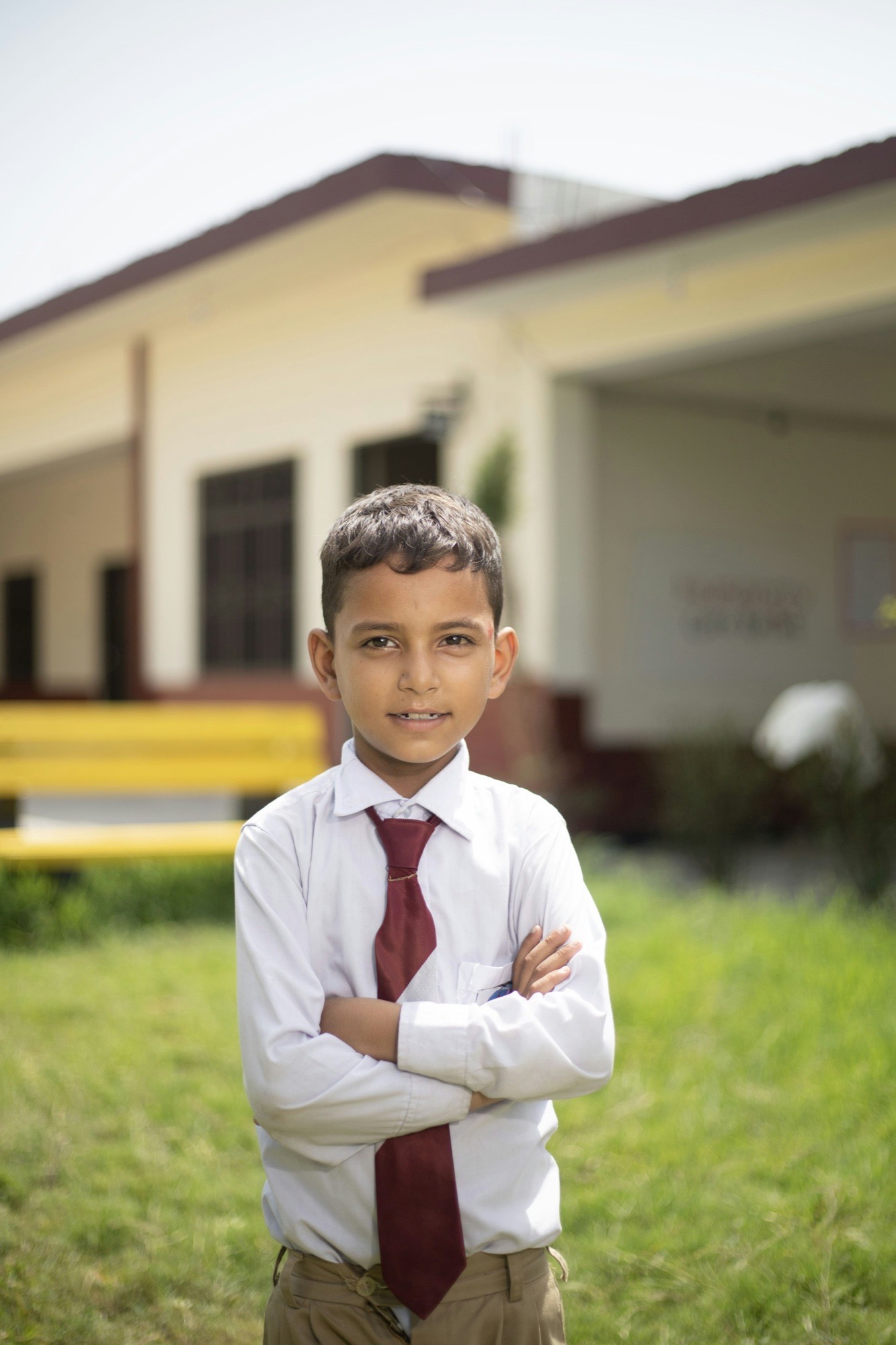 A schoolboy in a white shirt and maroon tie on the school lawn