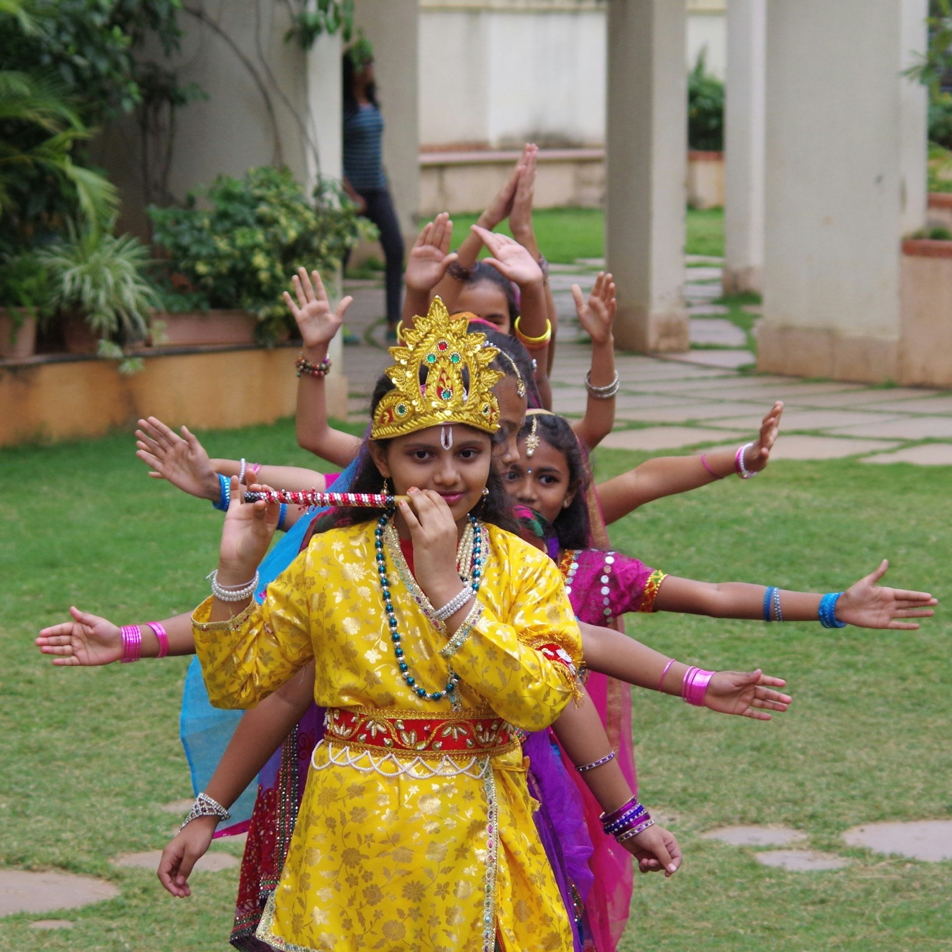 A girl dressed as Krishna with friends forming extra arms behind her