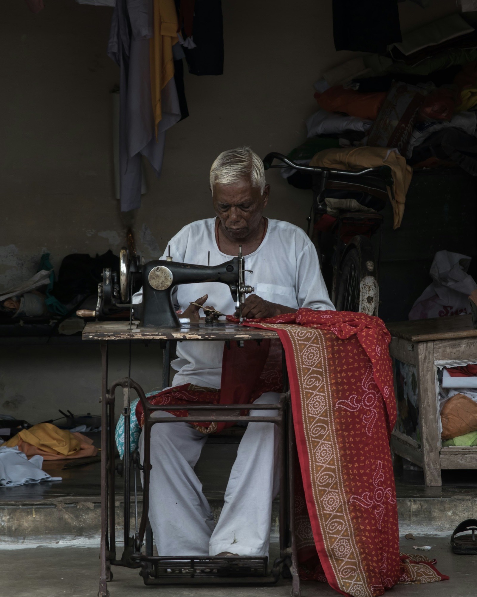 A tailor at a treadle sewing machine stitching printed fabric