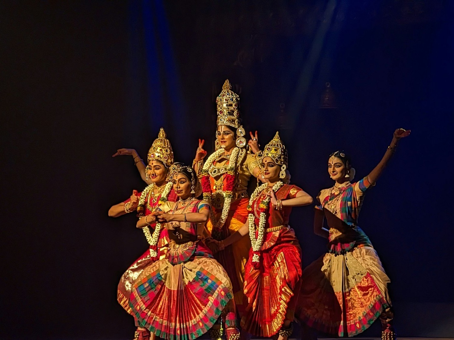 Classical dancers in matching costumes and gold crowns on a spotlit stage