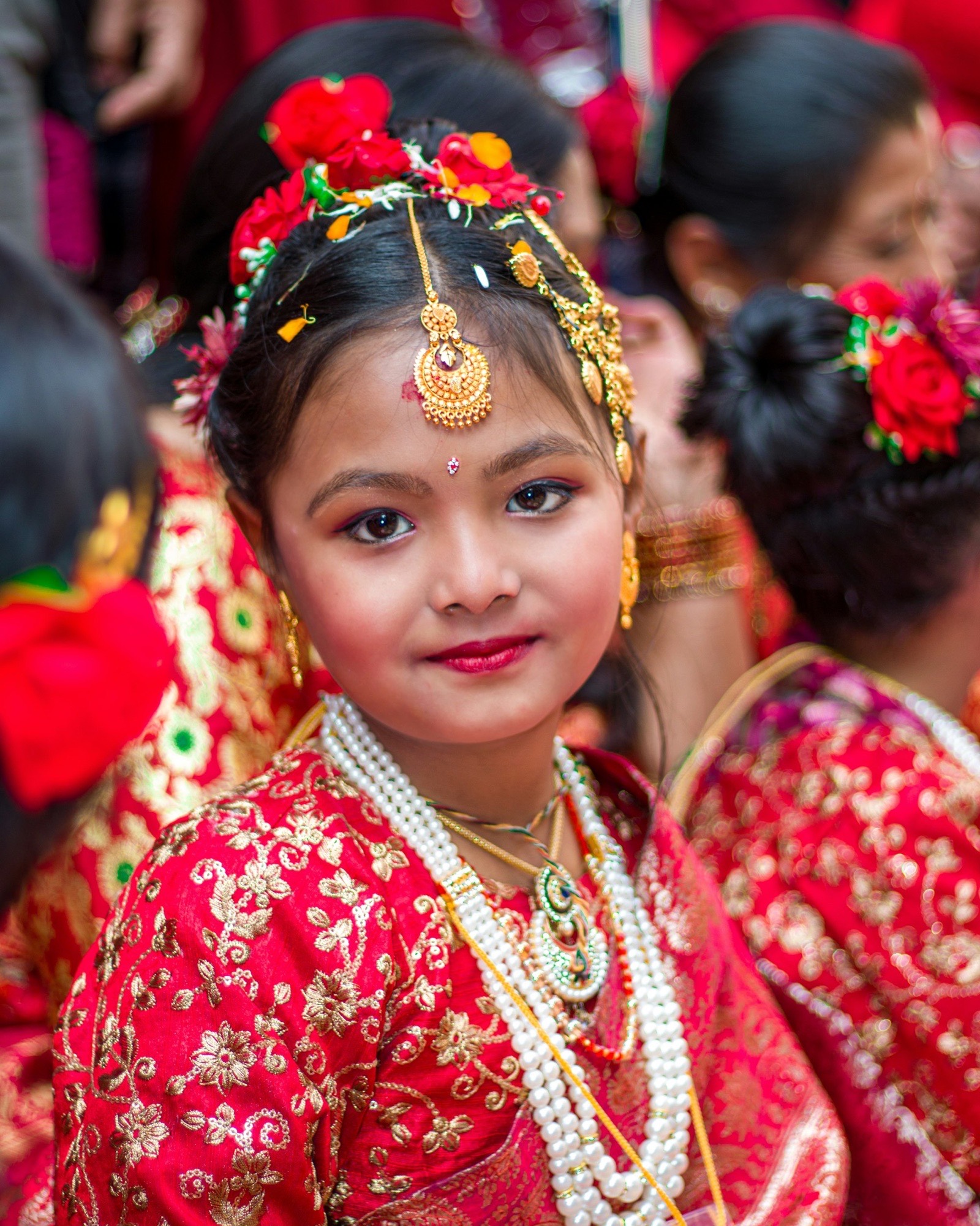 A young girl in a red-and-gold costume with flowers in her hair